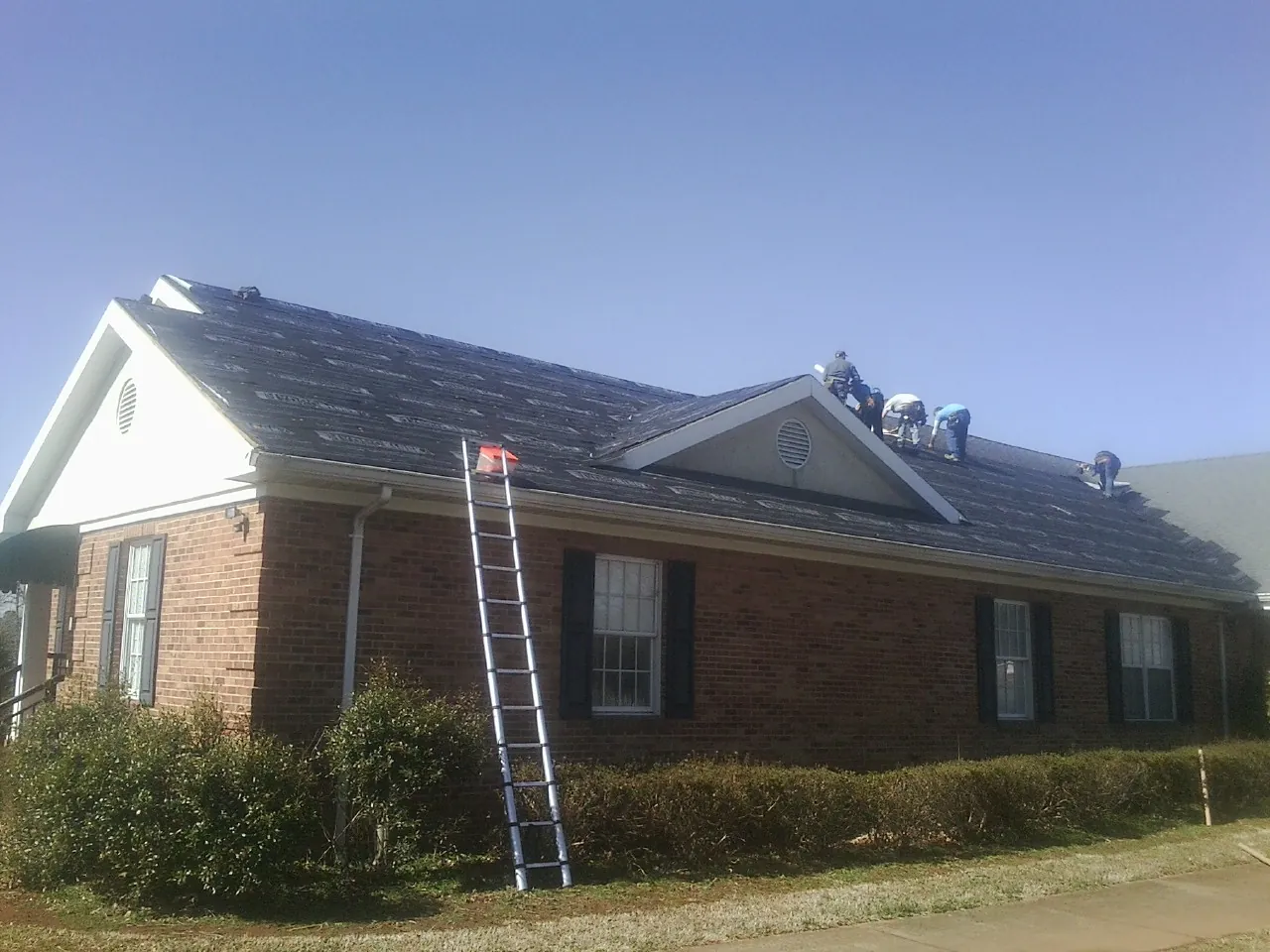 Crew tearing shingles off a brick ranch roof with a ladder set — Metal Roof Repair work by our crew in Wolfeboro