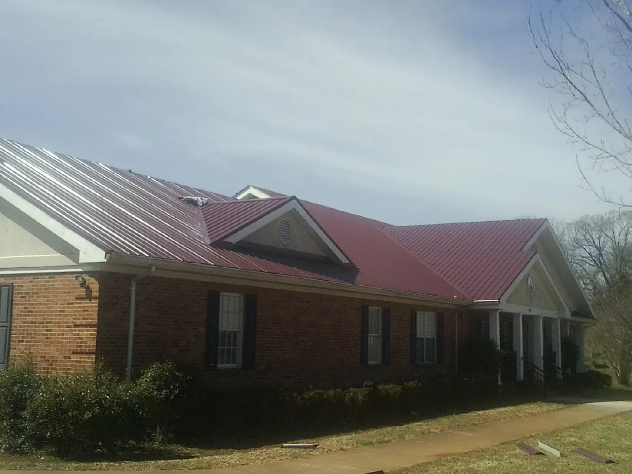 Red metal roof with gabled entries on a long brick building, from a Hail Damage Roof Repair job in Wolfeboro