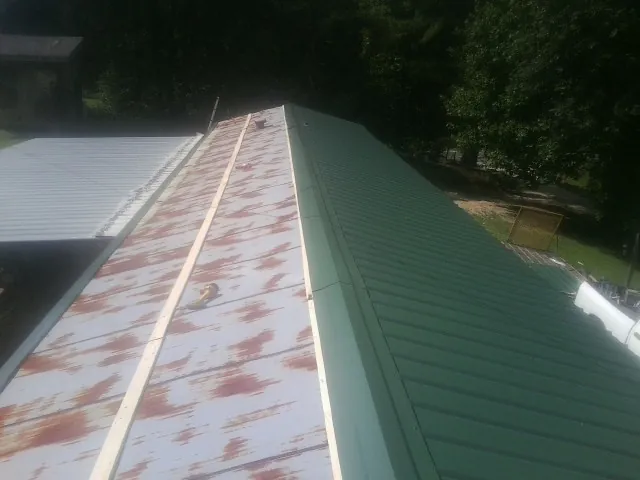 Old rusted panels beside newly installed green metal roofing — Wind Damage Roof Repair by Roofing Brothers in Wolfeboro