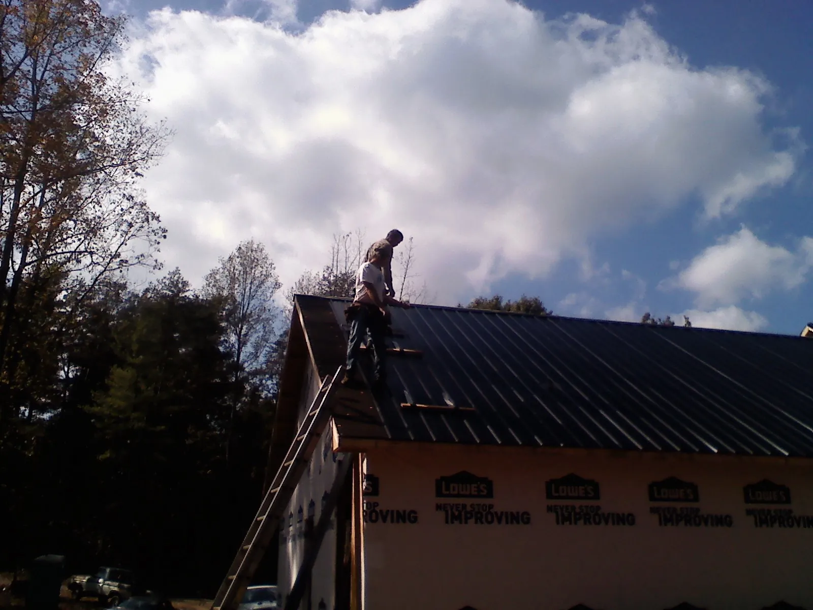 Roofer fastening dark metal panels high against a cloudy sky, from a Roof Inspection job in Wolfeboro