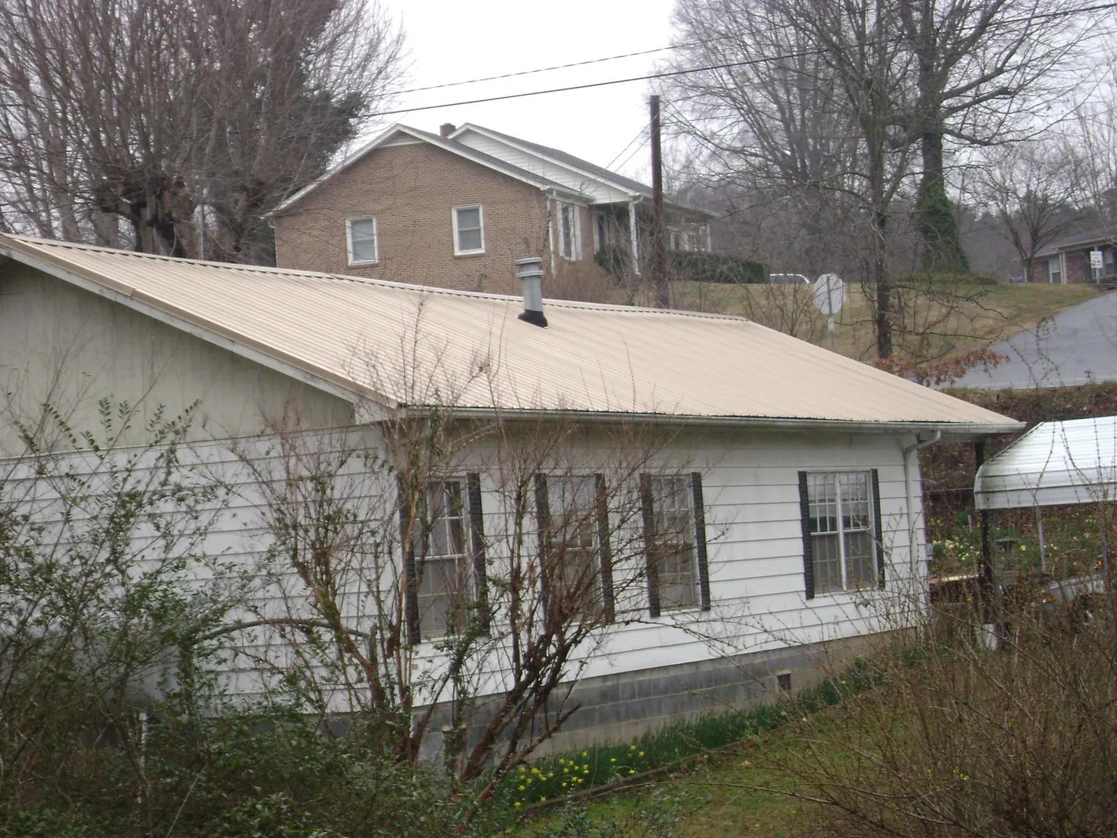 Tan metal roof on a white sided house set into a hillside — Commercial Roofing by Roofing Brothers in Wolfeboro