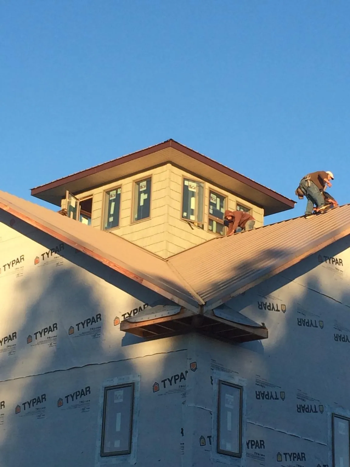 Roofers working around a rooftop cupola on a new metal roof at sunset — Roof Waterproofing in Wolfeboro by Roofing Brothers